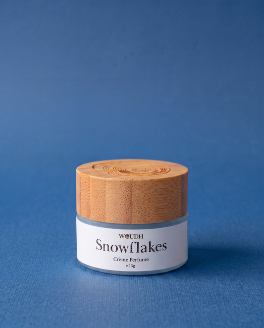A small cosmetic jar labeled 'WOUOH Snowflakes Crème Perfume' with a light wood-grain lid and white label, set against a solid blue background.